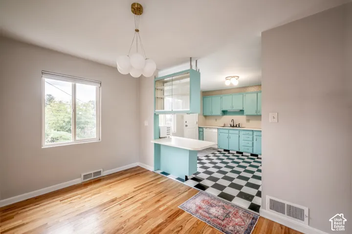 Dining area featuring wood-finish flooring and a multi-globe pendant light, offset by a kitchen with a checkerboard floor, built-in breakfast bar, and glass-front cabinetry
