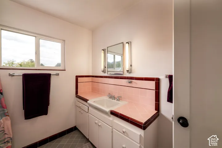 Vanity featuring custom-fitted ceramic tile countertop with contrast border, integrated sink basin, white cabinetry, dual vertical wall-mounted lighting fixtures, and ceramic tile flooring