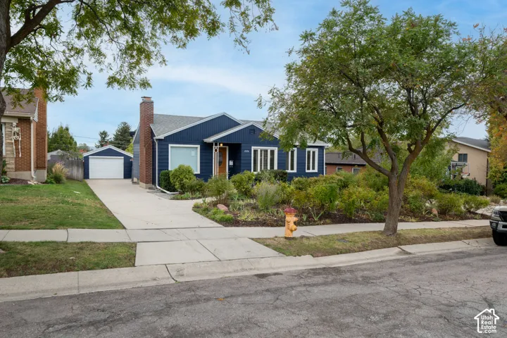 Exterior facade featuring horizontal lap siding, a brick chimney, a concrete driveway, a detached garage, and mature landscaping