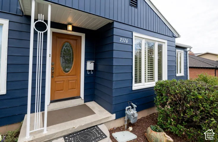 Exterior featuring dark lap siding, a wood-finish front door with an oval glass insert, decorative metal porch column, and multi-pane window configuration