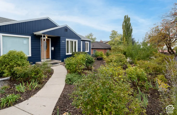 Blue horizontal siding exterior featuring a concrete walkway, mulched garden beds, and mature landscaping