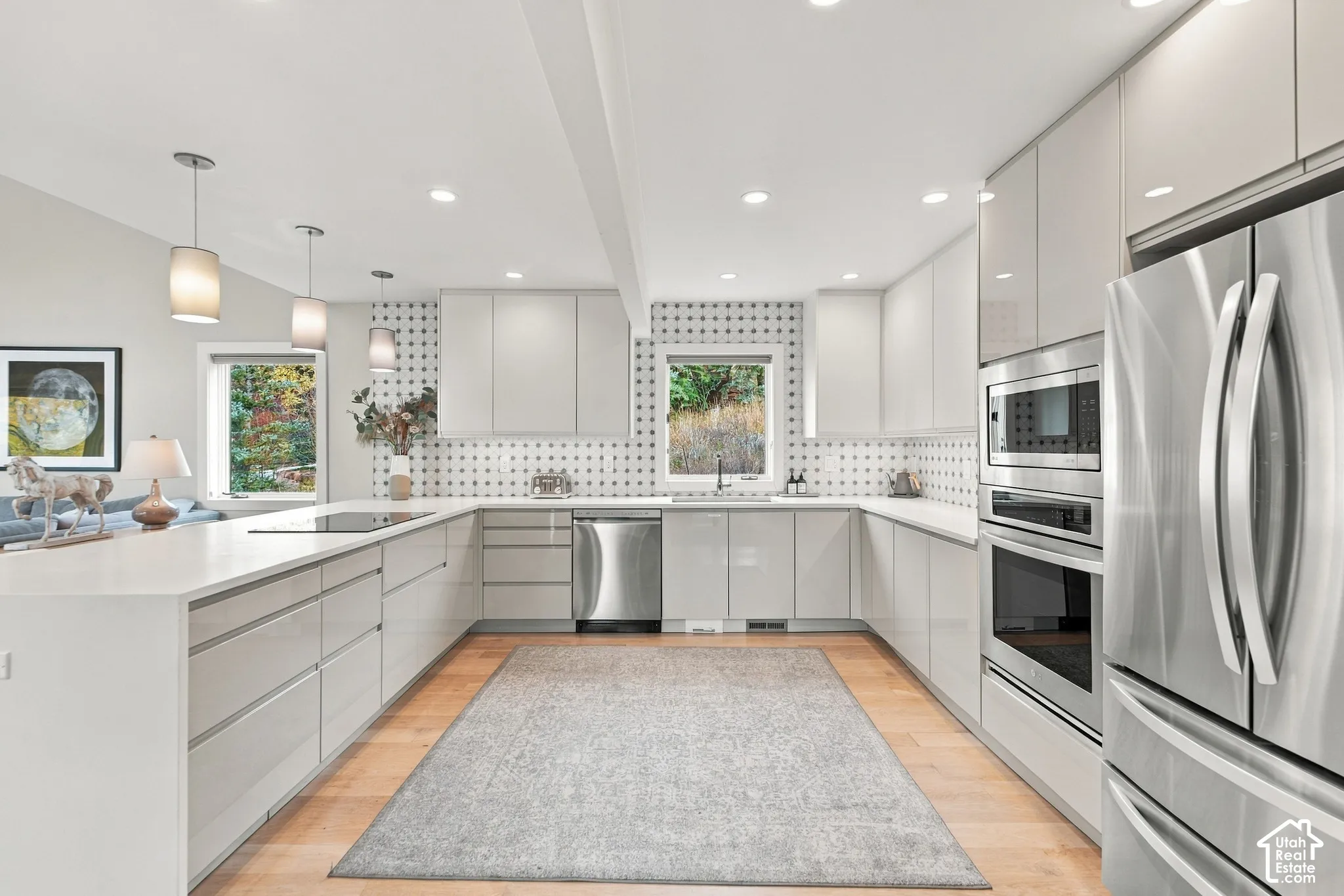 Contemporary kitchen featuring high-gloss cabinetry, stainless steel appliances, geometric tile backsplash, stone-surface countertops, and wood-finish flooring