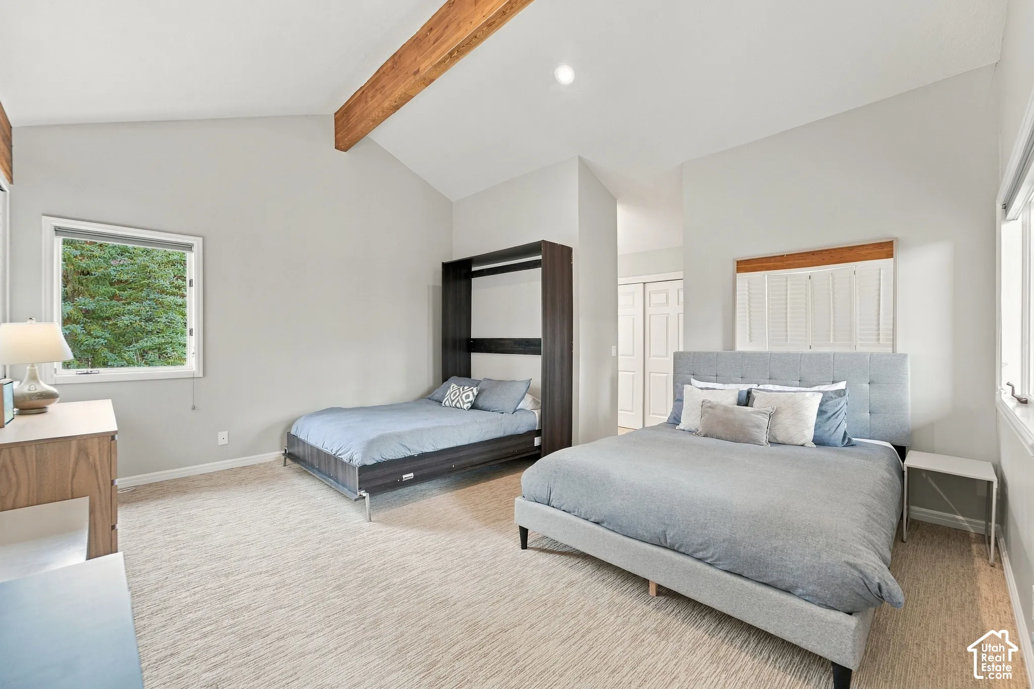 Vaulted ceiling with exposed wood beam, carpeted flooring, and neutral wall tones
