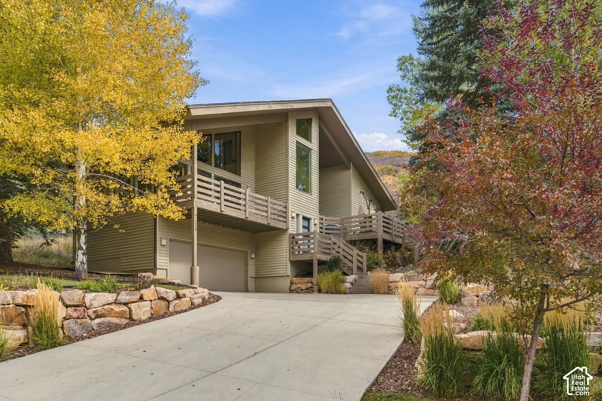 Multi-level home featuring horizontal siding, expansive multi-tier wooden balconies, integrated two-car garage, and terraced natural stone retaining walls