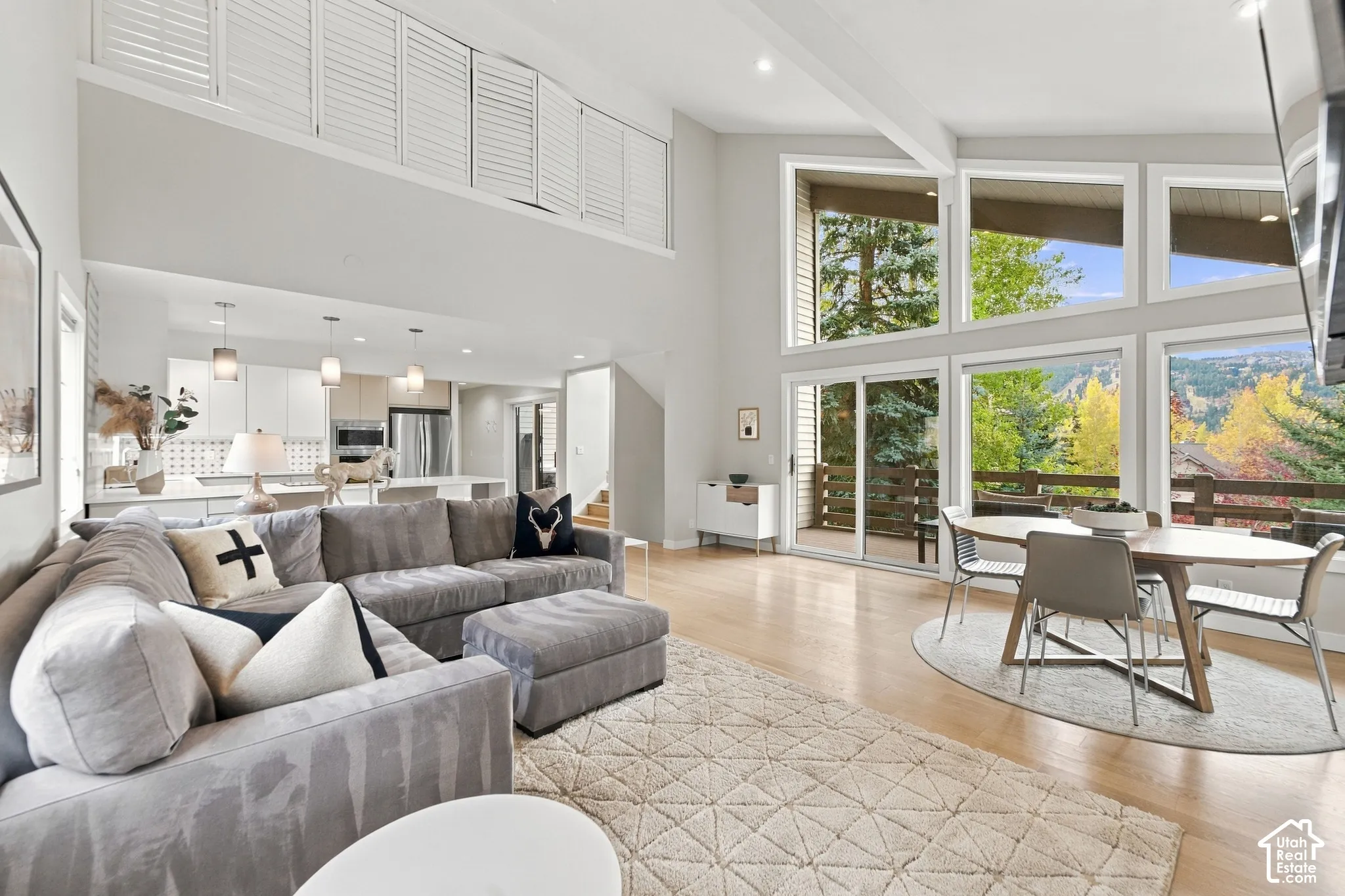 Vaulted ceilings featuring white architectural beams, floor-to-ceiling windows, wood-finish flooring, plantation-style shutters, and built-in recessed lighting