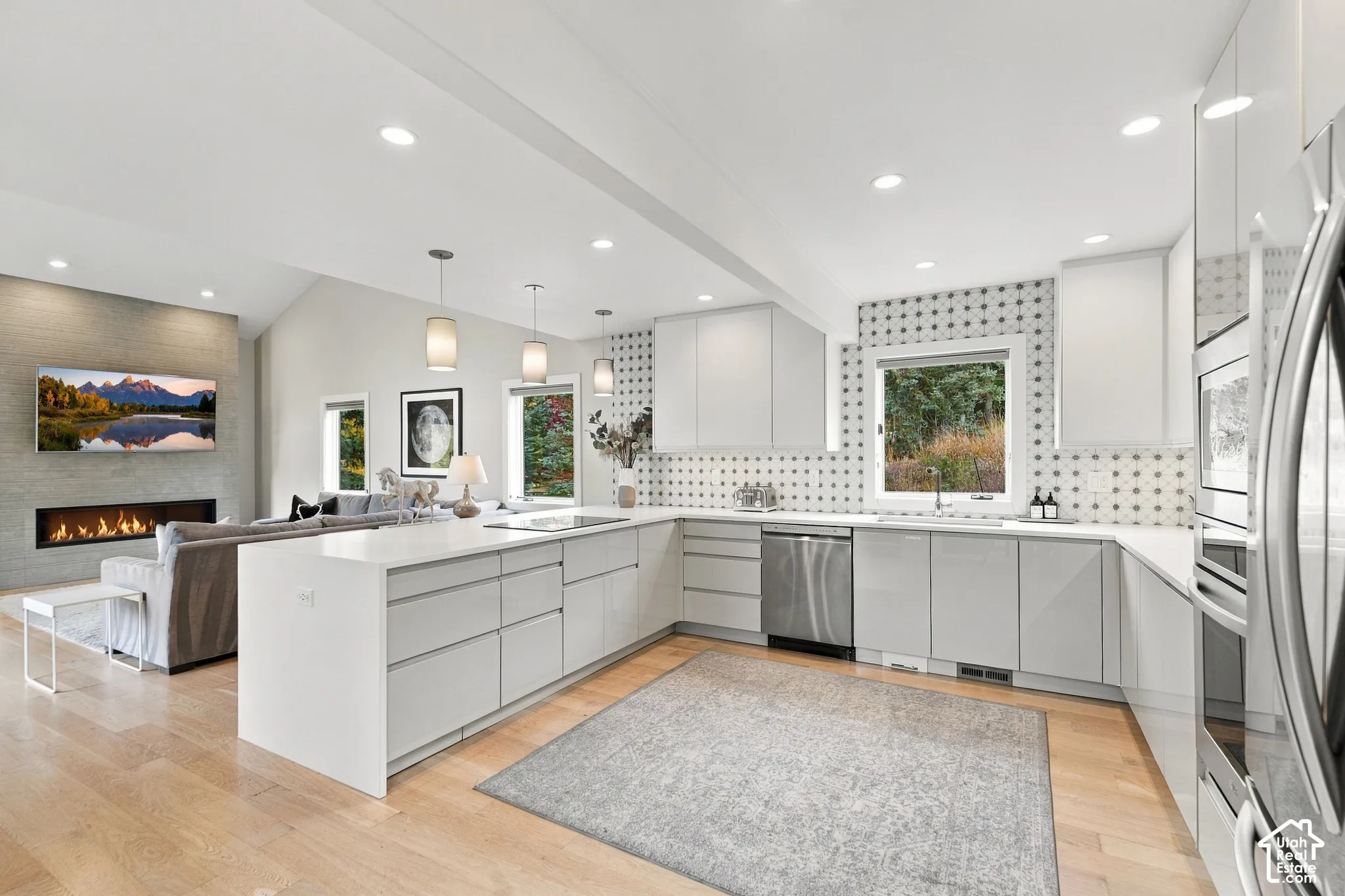 Modern kitchen featuring glossy flat-panel cabinetry, white solid-surface countertops, stainless steel appliances, patterned wall tile, and wood-finish flooring