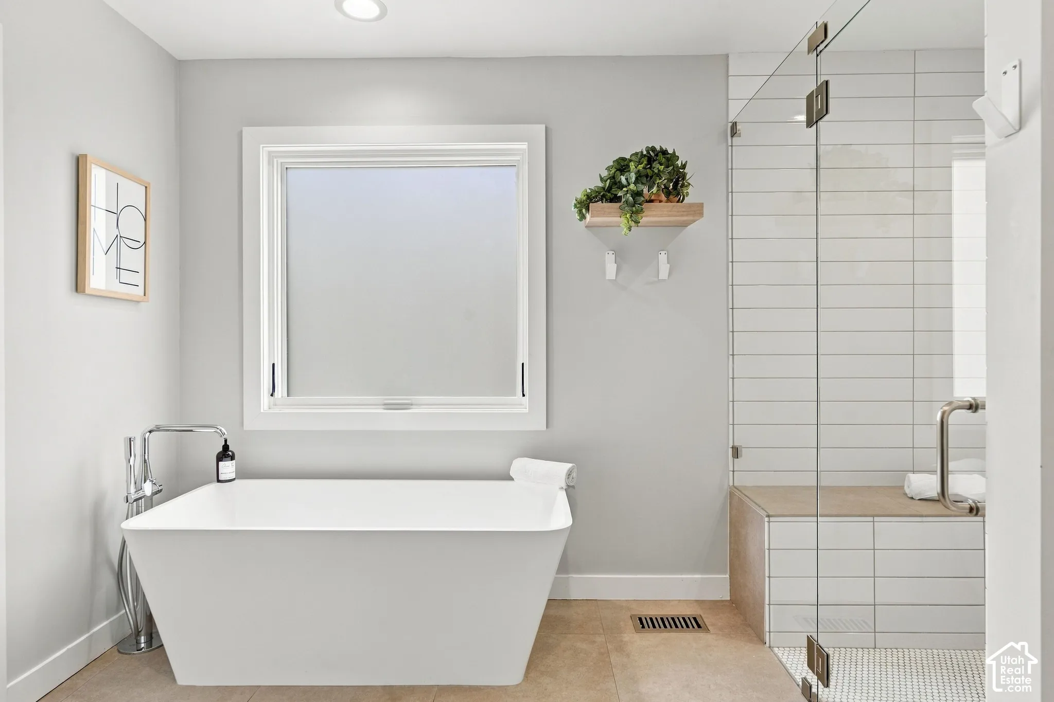 Freestanding soaking tub with floor-mounted chrome faucet, glass-enclosed shower with tiled bench, and large-format tile flooring