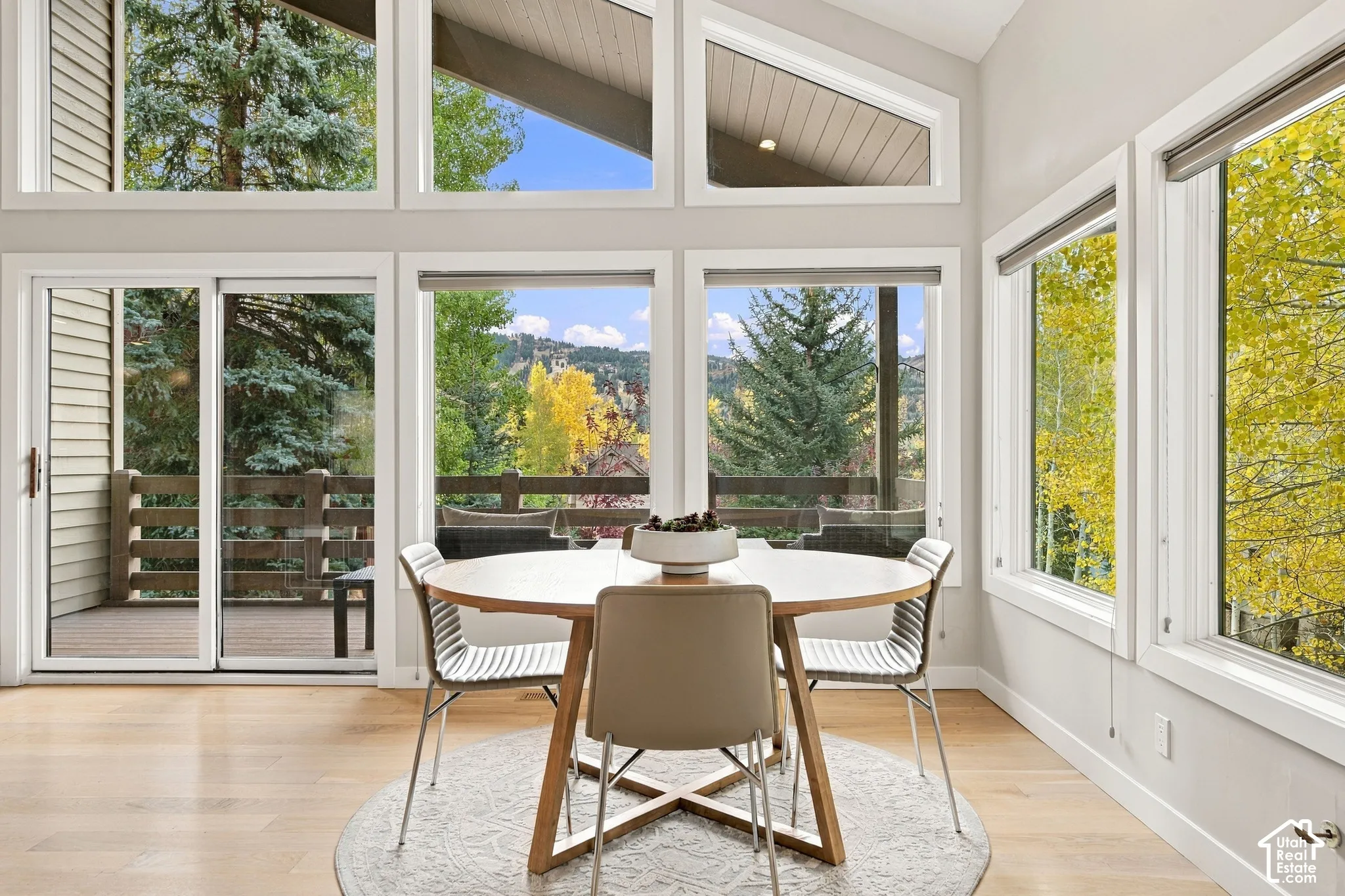 Vaulted ceilings featuring expansive floor-to-ceiling windows, wood-finish flooring, and a sliding glass door providing access to a wooden deck