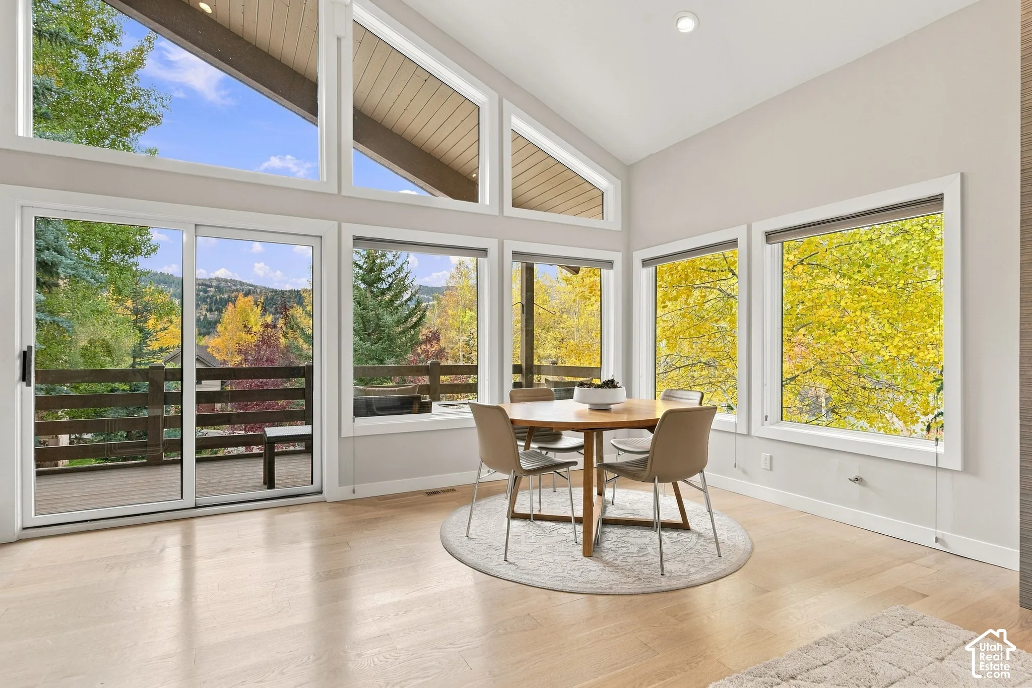 Vaulted ceilings with wood-plank finish, large floor-to-ceiling windows, light-tone wood-finish flooring, and sliding glass door access to a private exterior deck