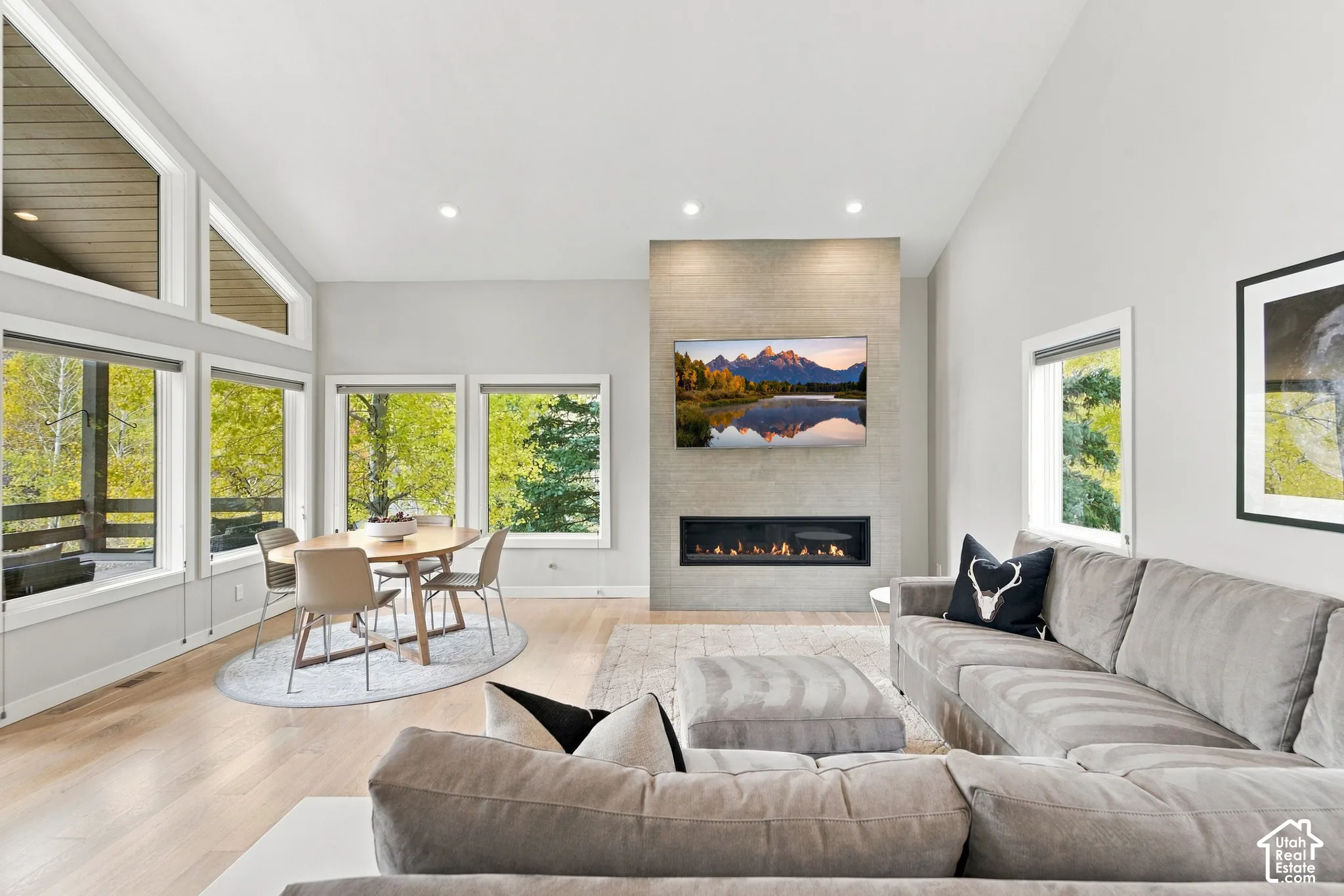 Vaulted ceilings, expansive windows, light-toned wood-finish flooring, and a floor-to-ceiling stone-surround fireplace with a linear insert