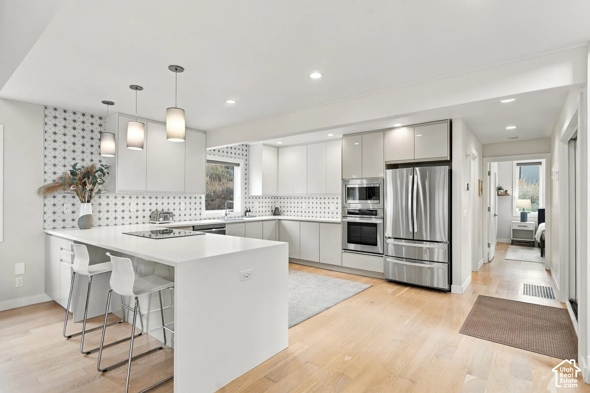Kitchen featuring gloss-finish cabinetry, geometric tile backsplash, quartz countertops, integrated stainless steel appliances, and wood-finish flooring
