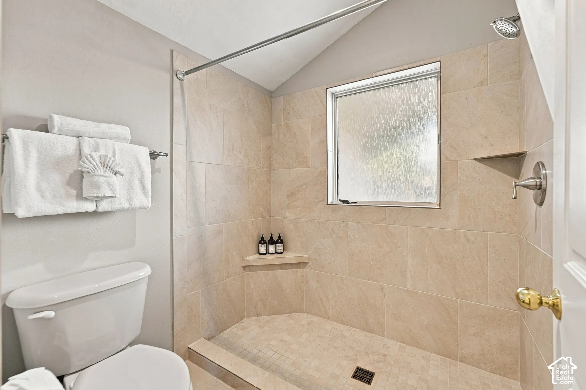 Walk-in shower featuring floor-to-ceiling neutral tile, integrated corner shelving, a window, and a built-in metal faucet fixture
