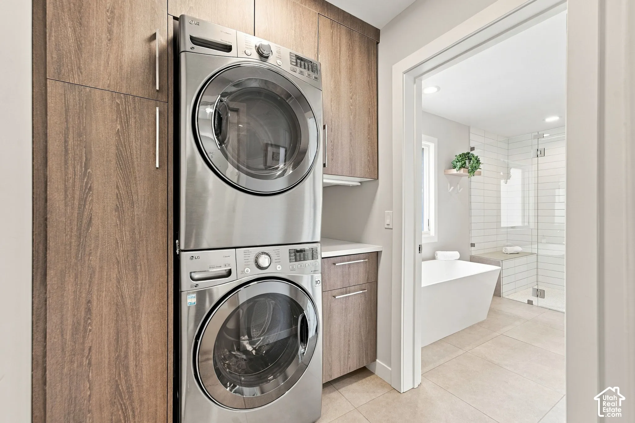Stacked stainless steel laundry appliances, custom wood-finish cabinetry, stone-surface countertop, and ceramic tile flooring