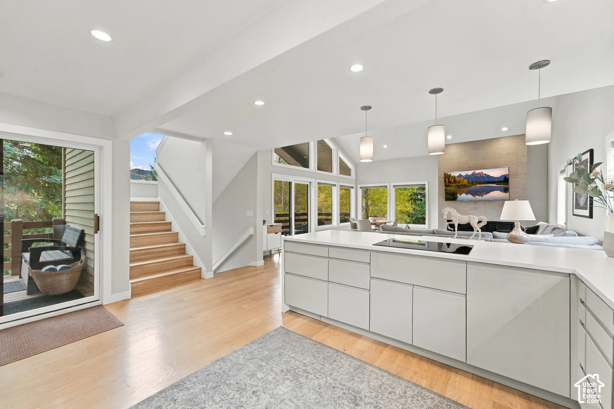 Open-concept kitchen featuring gloss-finish cabinetry, a white countertop with an inset cooktop, wood-finish flooring, vaulted ceilings with recessed lighting, and expansive windows