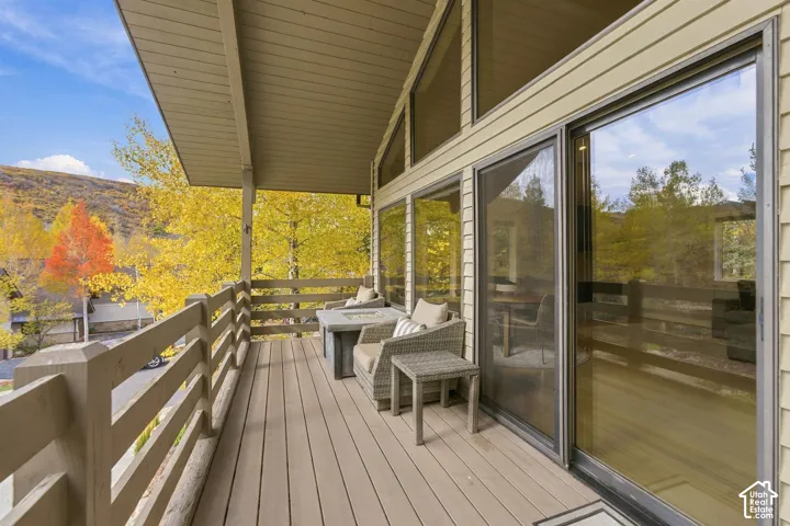 Covered deck featuring wood-finish decking, horizontal slat railing, and floor-to-ceiling glass sliding doors with transoms