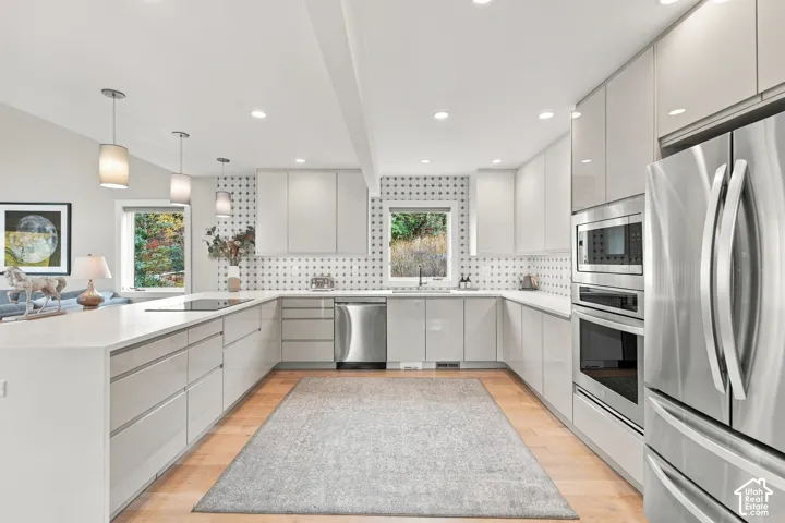 Contemporary kitchen featuring high-gloss cabinetry, stainless steel appliances, geometric tile backsplash, stone-surface countertops, and wood-finish flooring