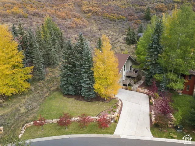 Residence featuring a multi-level wood deck, concrete driveway, stone retaining walls, and mature evergreen and deciduous landscaping