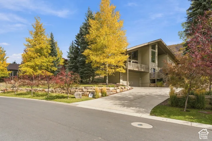 Contemporary residence with a vaulted roofline, elevated balcony with horizontal railing, concrete driveway, and tiered stone retaining walls