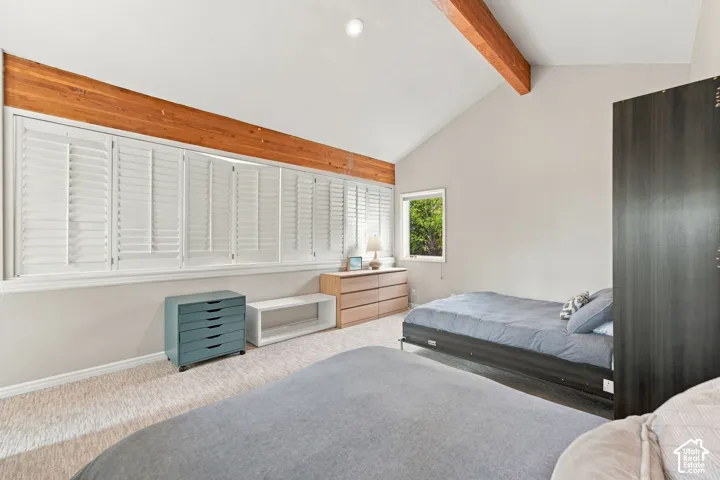 Vaulted ceiling featuring an exposed wood beam, large windows with white louvered plantation shutters, and wall-to-wall carpeting