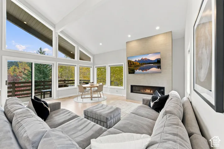 Vaulted ceilings with large windows, linear fireplace with a floor-to-ceiling stone surround, and wood-finish flooring