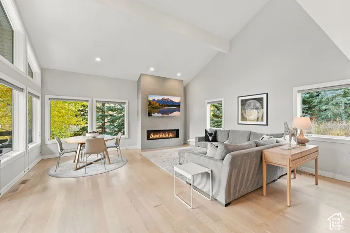 Vaulted ceilings, wood-finish flooring, linear fireplace with a textured tile surround, and large picture windows