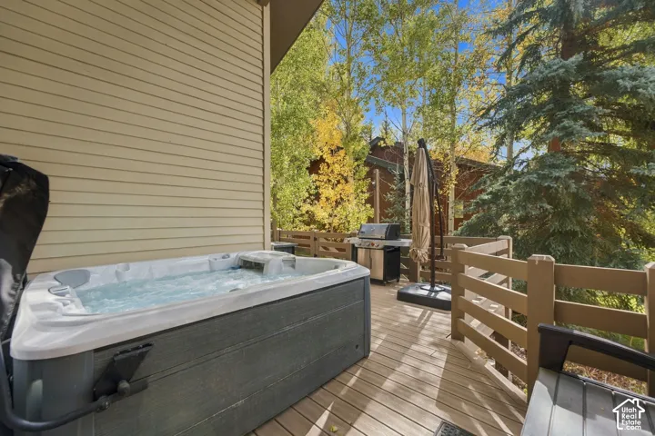 Multi-level wood deck featuring a built-in spa, horizontal wood railing, and mature evergreen and aspen trees