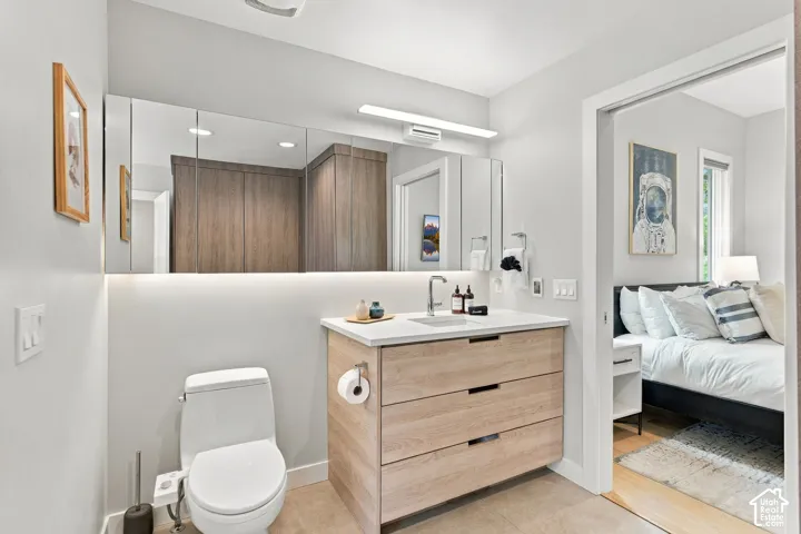 Vanity featuring a light wood finish, stone-surface countertop, rectangular undermount sink, and integrated LED under-cabinet lighting, complemented by a tri-panel mirrored medicine cabinet and wall-mounted linear light fixture