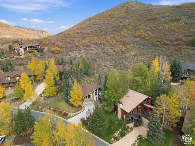 Multi-level residence featuring a pitched roofline, stone exterior cladding, covered balcony, and concrete driveway, situated against a mountainous landscape