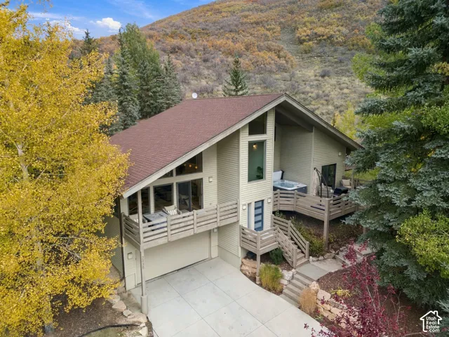 Contemporary residence featuring multi-level wooden decking, expansive floor-to-ceiling windows, attached garage, and a mountainous backdrop