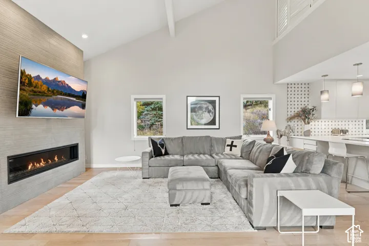 Vaulted ceiling featuring a linear fireplace with textured surround, wood-finish flooring, and pendant lighting