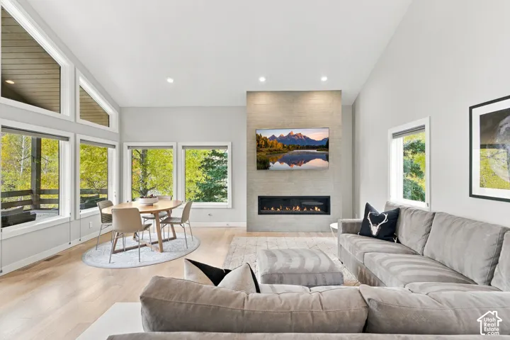 Vaulted ceilings, expansive windows, light-toned wood-finish flooring, and a floor-to-ceiling stone-surround fireplace with a linear insert