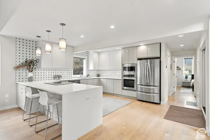 Kitchen featuring gloss-finish cabinetry, geometric tile backsplash, quartz countertops, integrated stainless steel appliances, and wood-finish flooring