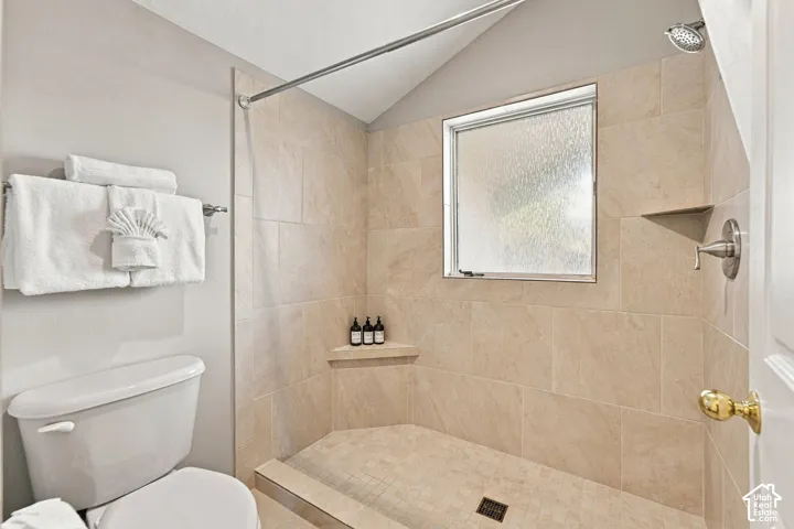 Walk-in shower featuring floor-to-ceiling neutral tile, integrated corner shelving, a window, and a built-in metal faucet fixture