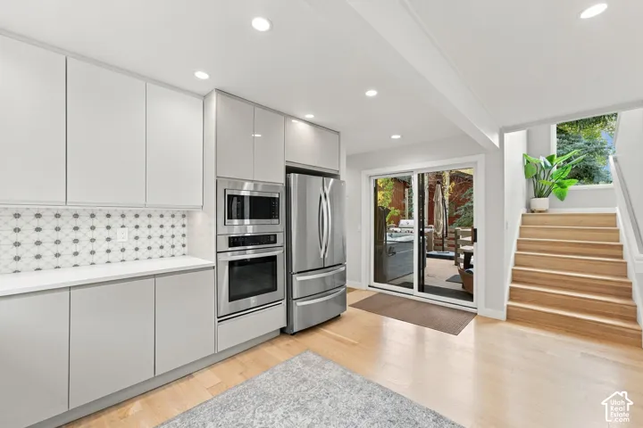 Kitchen featuring high-gloss cabinetry, stainless steel wall-mounted oven and microwave, patterned tile backsplash, recessed lighting, and wood-finish flooring