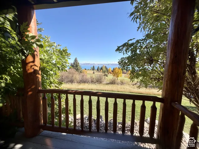 Covered porch featuring heavy timber columns, rustic wood railing, and expansive landscape scenery including a manicured lawn and water horizon