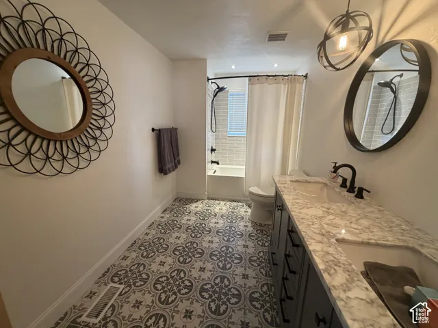 Bathroom featuring a dual-sink vanity with a stone-finish countertop, patterned tile flooring, matte black fixtures, and two circular mirrors