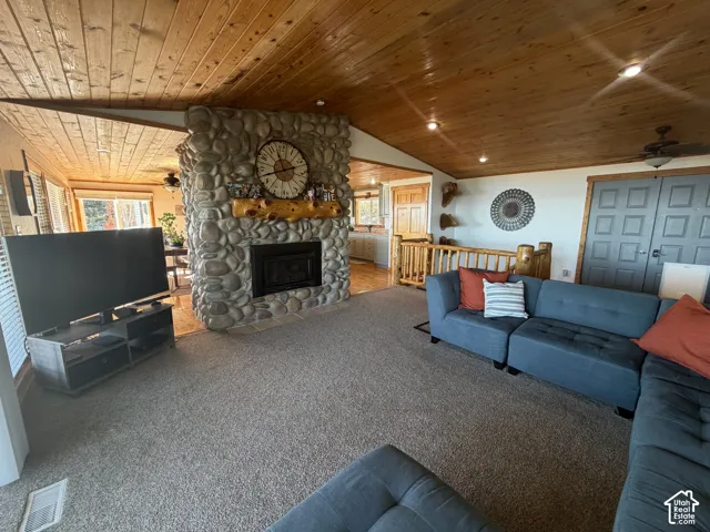 Vaulted wood-plank ceiling, natural stone fireplace with a thick timber mantel, recessed lighting, and wooden railing detail