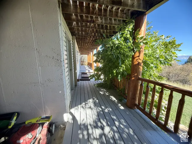 Covered exterior walkway featuring a wood-plank deck, exposed timber ceiling joists, and rustic log-style support posts and railing