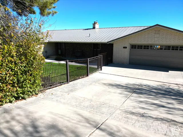 Single-story exterior featuring light-colored brick masonry, a standing-seam metal roof, a multi-car garage with transom windows, and a decorative metal perimeter fence