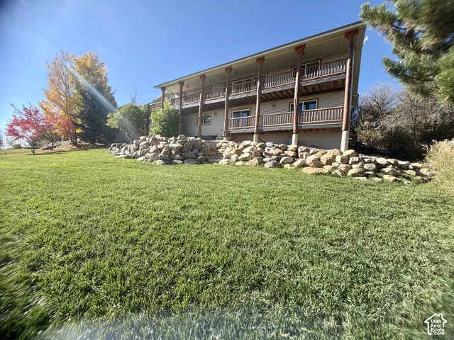 Two-story exterior featuring double-level covered balconies, exposed wood posts, natural stone retaining wall, and expansive lawn