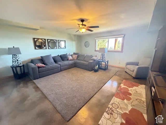 Living area featuring polished concrete flooring, recessed lighting, a ceiling fan with integrated light fixture, and a single-pane window with wood trim