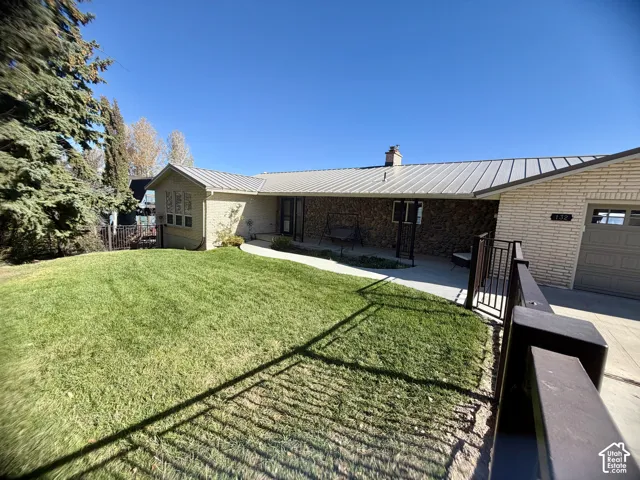 Single-story brick exterior featuring a metal roof, stone facade accents, concrete patio, and fenced lawn area