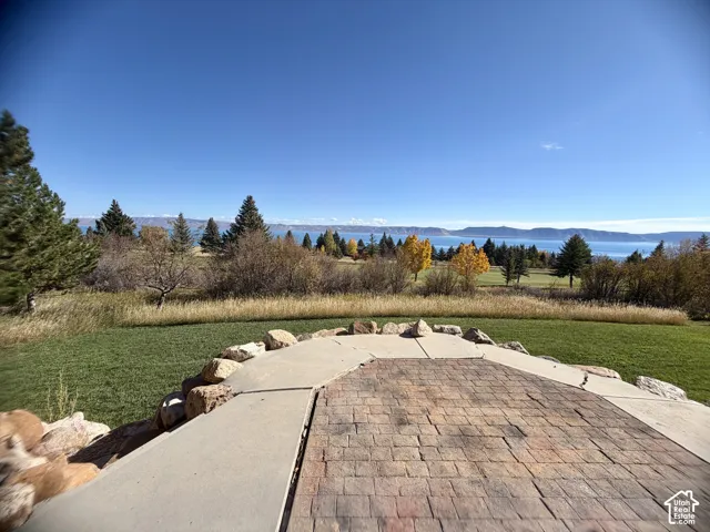 Paver patio featuring a concrete border and natural stone edging, overlooking a grass lawn and distant water