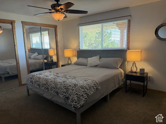 Room featuring large mirrored closet doors with natural wood trim, sliding windows with horizontal blinds, and a ceiling fan with integrated lighting