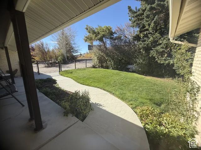 Covered concrete patio with a winding pathway, manicured lawn, and perimeter metal fencing