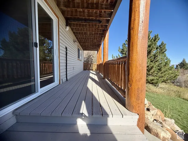 Covered deck featuring horizontal wood decking, rustic log support posts, and a matching log railing, with horizontal siding and sliding glass doors