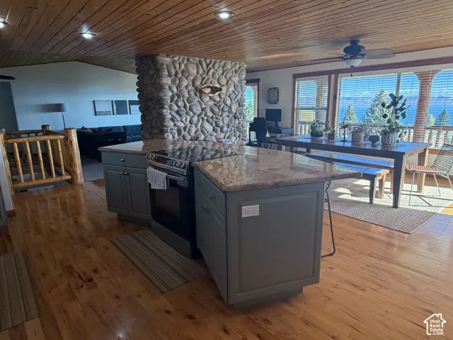 Kitchen featuring a central island with a stone-surface countertop, integrated range, wood-finish flooring, custom wood-plank ceiling, and a prominent river-stone chimney feature