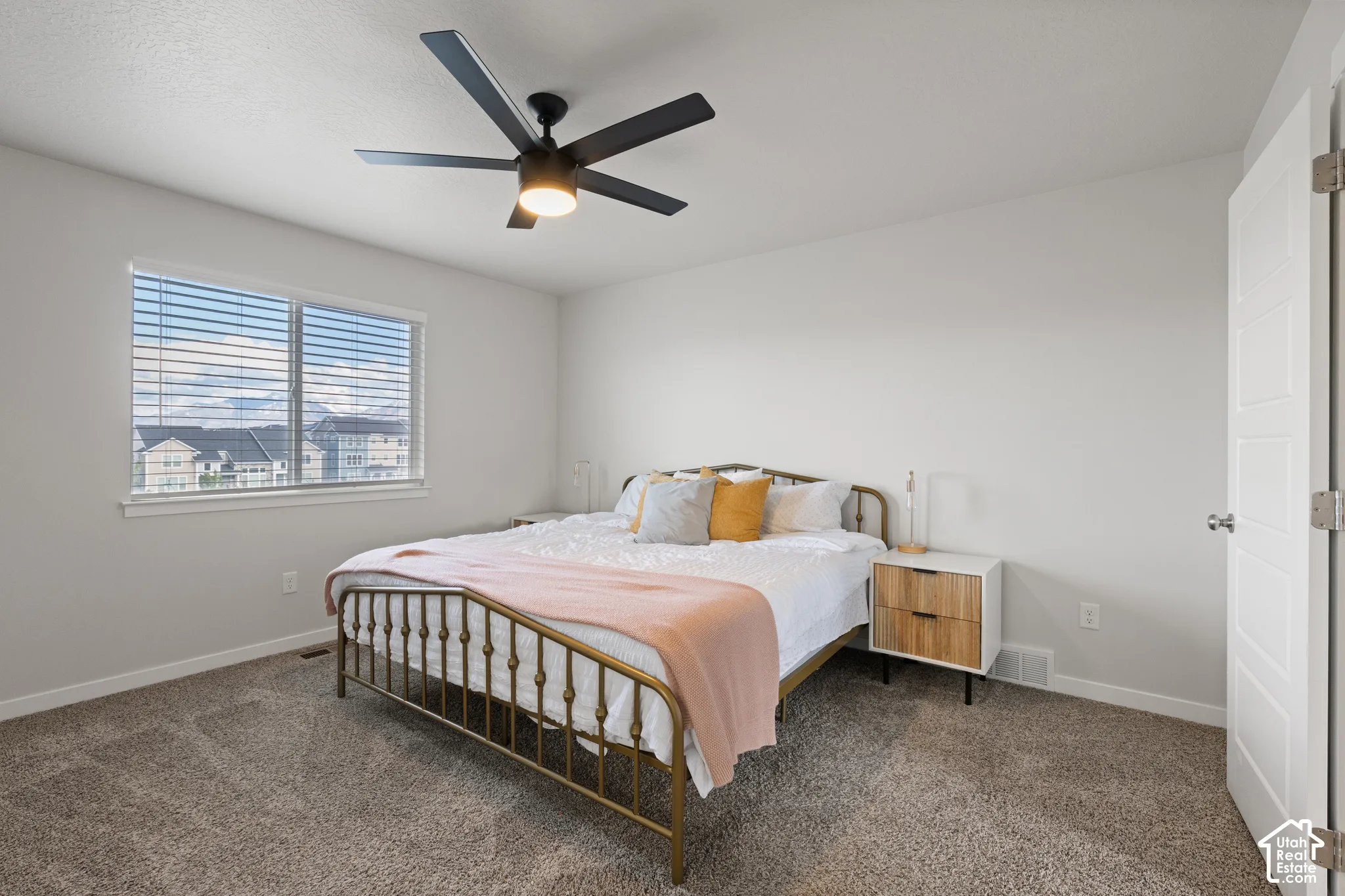 Neutral-toned interior featuring wall-to-wall carpeting, a matte black five-blade ceiling fan with integrated lighting, and a window with horizontal blinds