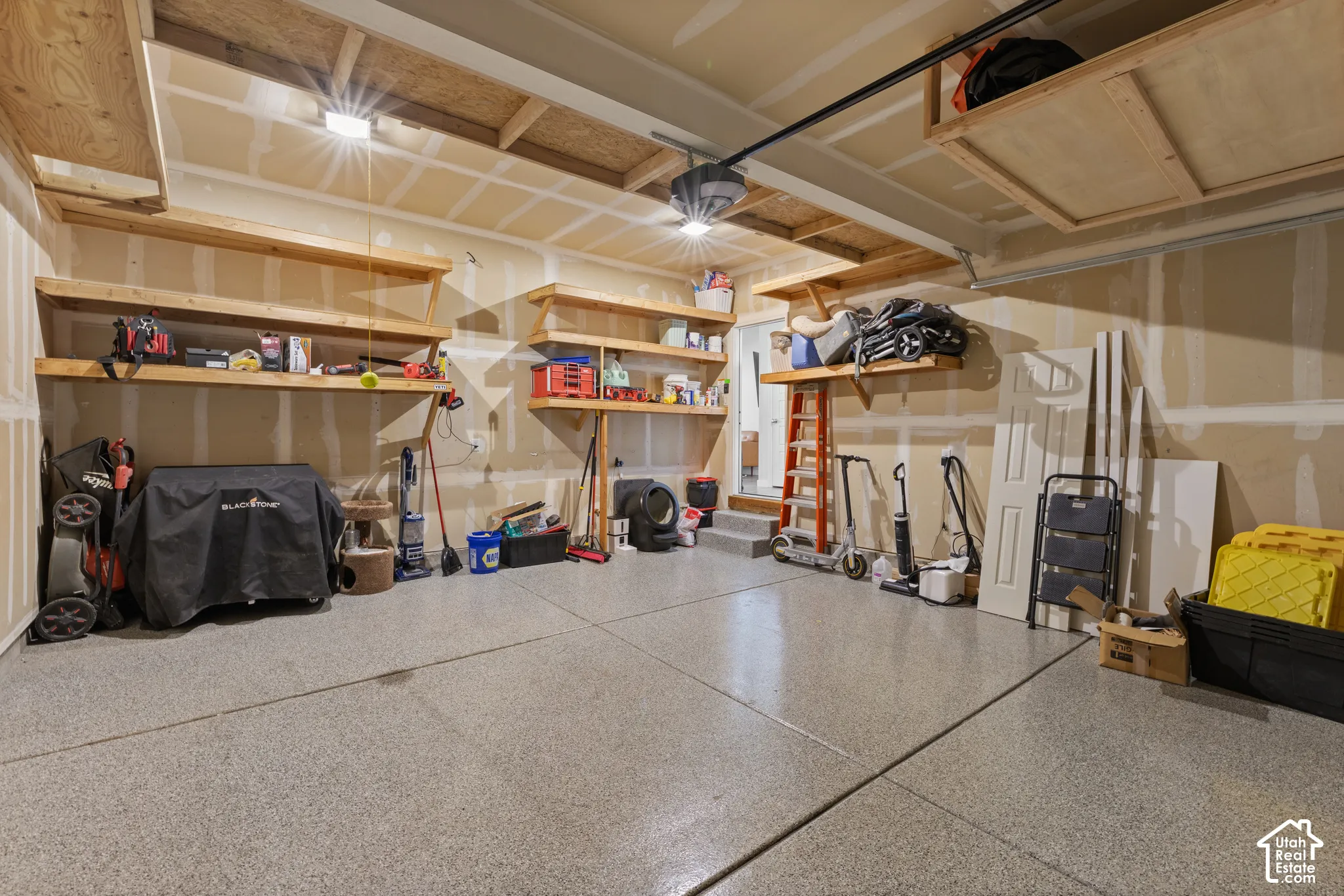 Garage featuring epoxy-coated concrete flooring, custom built-in wooden wall shelving, and overhead storage platforms