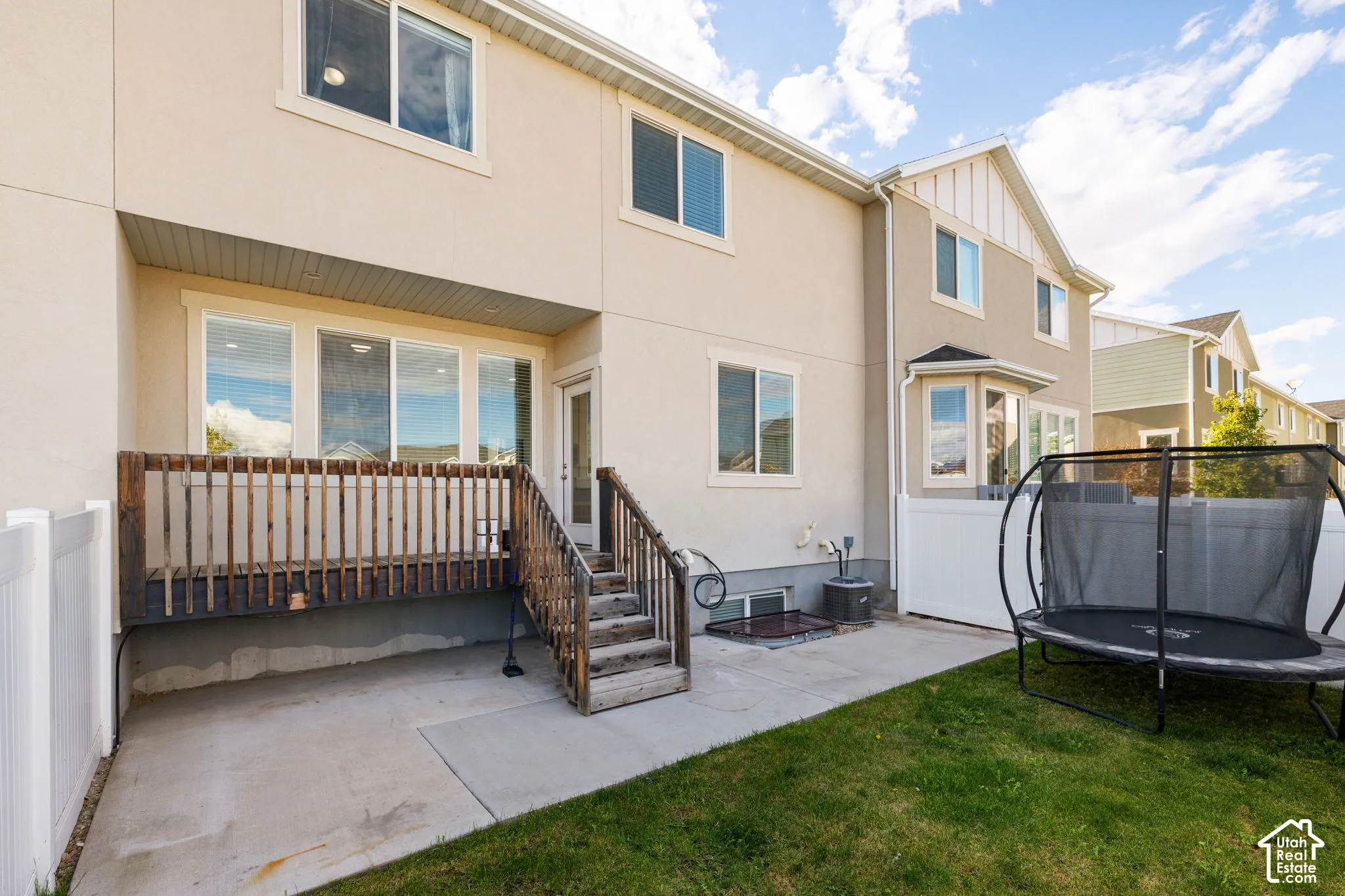 Exterior rear elevation featuring stucco siding, elevated wood deck with stairs, concrete patio, and white vinyl perimeter fencing